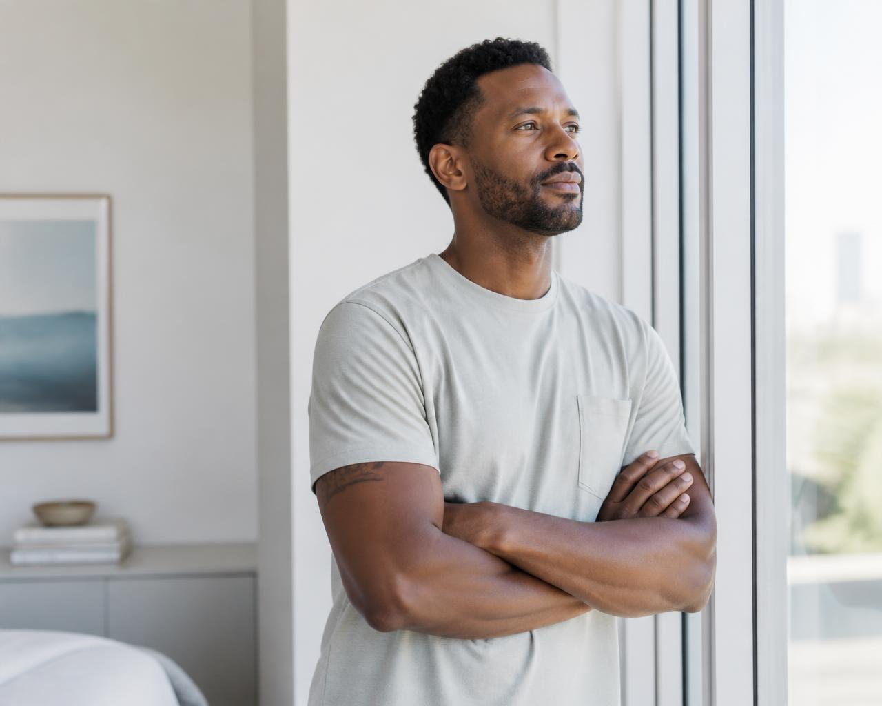 A man standing by a sunlit window in a calm modern home, looking thoughtful